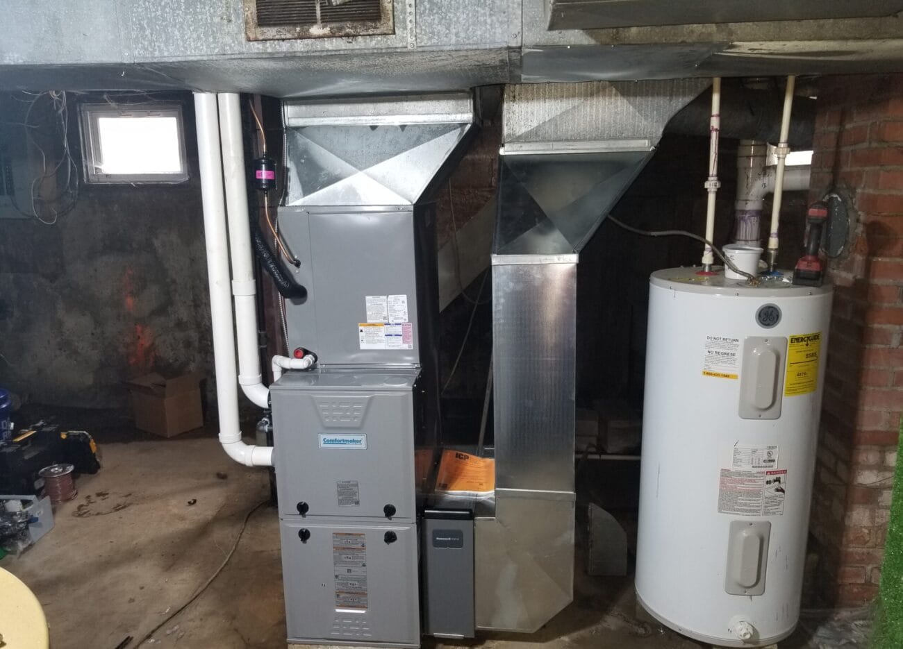 A basement with a furnace, ductwork, and a water heater installed next to each other against a brick wall.